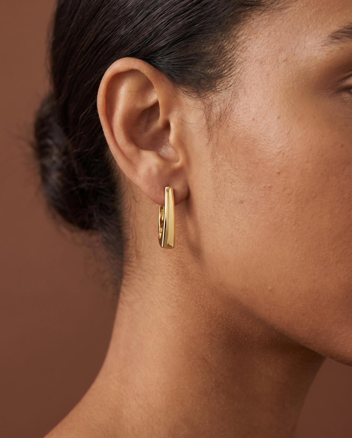 Golden Hour Huggie Earrings worn on the ear, polished tapered gold
